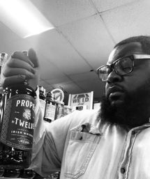 Person with glasses and beard examining a bottle of Irish whiskey in a liquor store aisle, retail shelves and a 'We I.D.' sign visible in the background