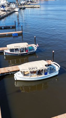 Two covered tour boats docked at a sunny Milwaukee marina, tied to wooden piers with calm blue water and reflections.