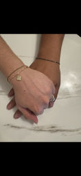 Two hands clasped on a white marble countertop, one wearing stacked gold bracelets with a small clover charm and the other wearing a thin chain bracelet and a sparkling diamond ring.