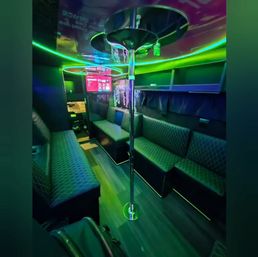Vibrant neon-lit party bus interior with a chrome dance pole, quilted bench seating along both sides, overhead green-blue LED accent lighting and a wall TV — modern mobile lounge.