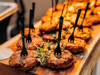 Golden-brown crab cake appetizers topped with microgreens and black cocktail forks on a wooden serving board, buffet-style seafood catering