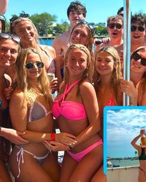 Smiling group of friends at a sunny boat party in colorful bikinis, holding drinks with a coastal marina and palm trees in the background.