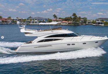 White luxury motor yacht cruising a palm-lined coastal inlet past waterfront mansions, leaving a foamy wake