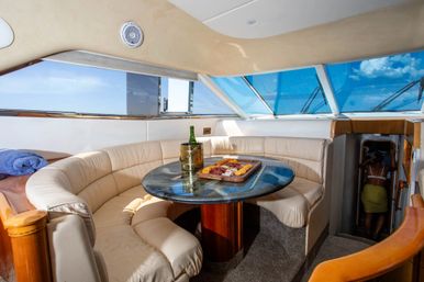 Luxury yacht dining salon with curved cream leather banquette, round blue-glass table topped with a charcuterie board and chilled wine, panoramic blue-tinted windows and ocean sky view.