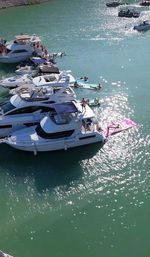 Sunlit turquoise cove with luxury yachts moored side-by-side and people relaxing on inflatables and swim platforms