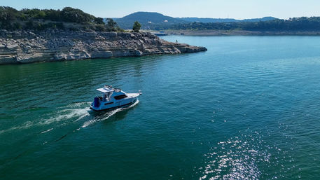 White motorboat cruising across a clear blue lake past layered limestone cliffs and tree‑topped hills under a sunny sky