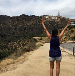 Visitor with arms raised on a dusty trail overlooking the Hollywood sign on the hills of Los Angeles