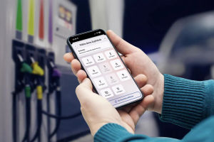 Person steht vor Zapfsäule und blickt auf Smartphone. Das Smartphone zeigt das geöffnete Tanken Feature in der Bluecode App.