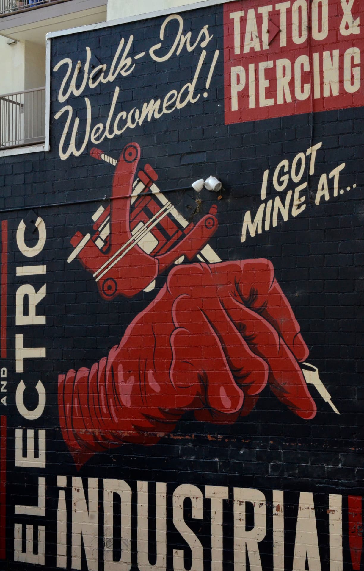 The side wall of Industrial Piercing in Berkeley, showing their name and a retro-style illustration of a hand holding a tattoo gun