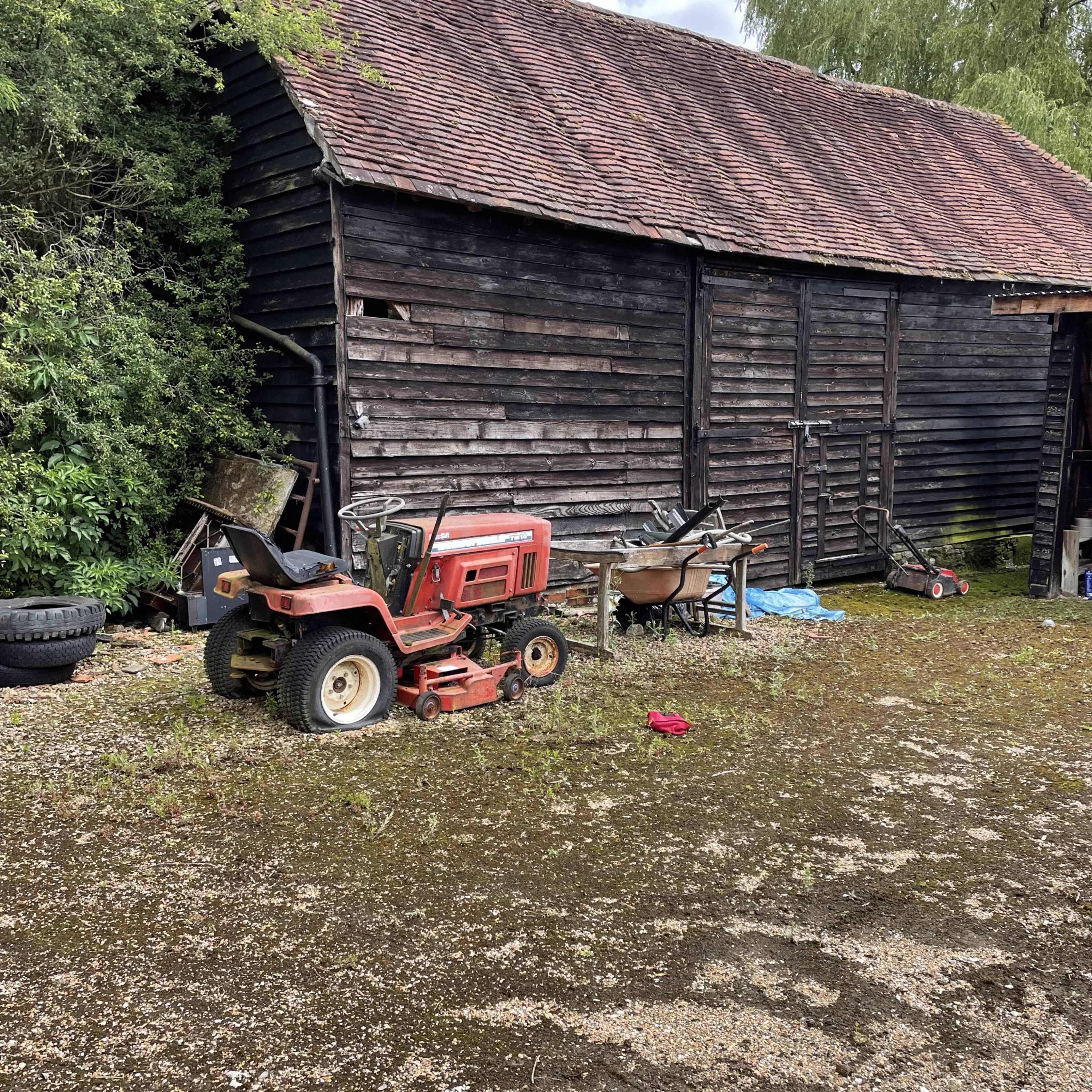 An outbuilding with a ride-on mower and garden equipment to be cleared