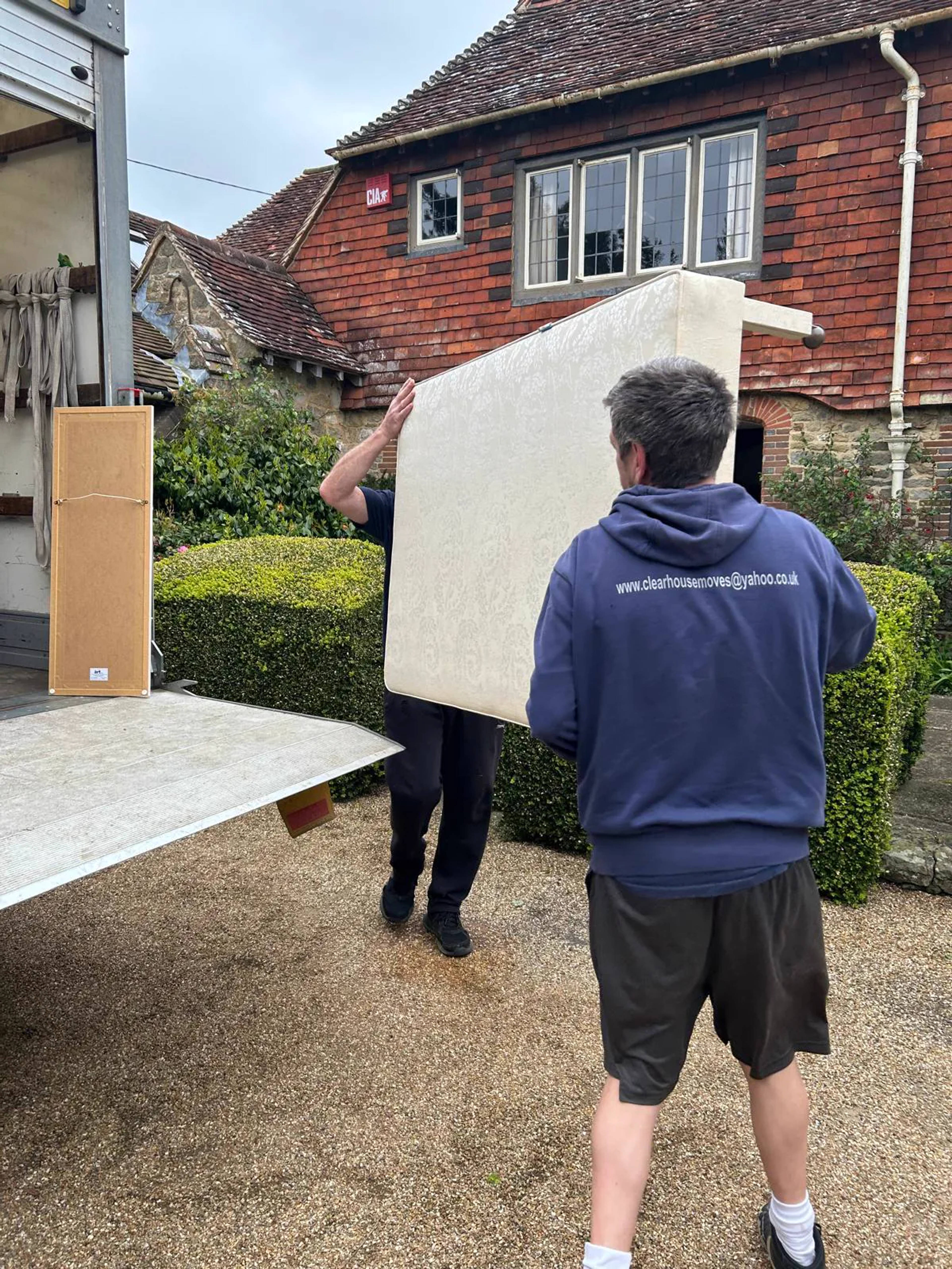 Two Clear House Moves movers carrying a mattress into a removal van