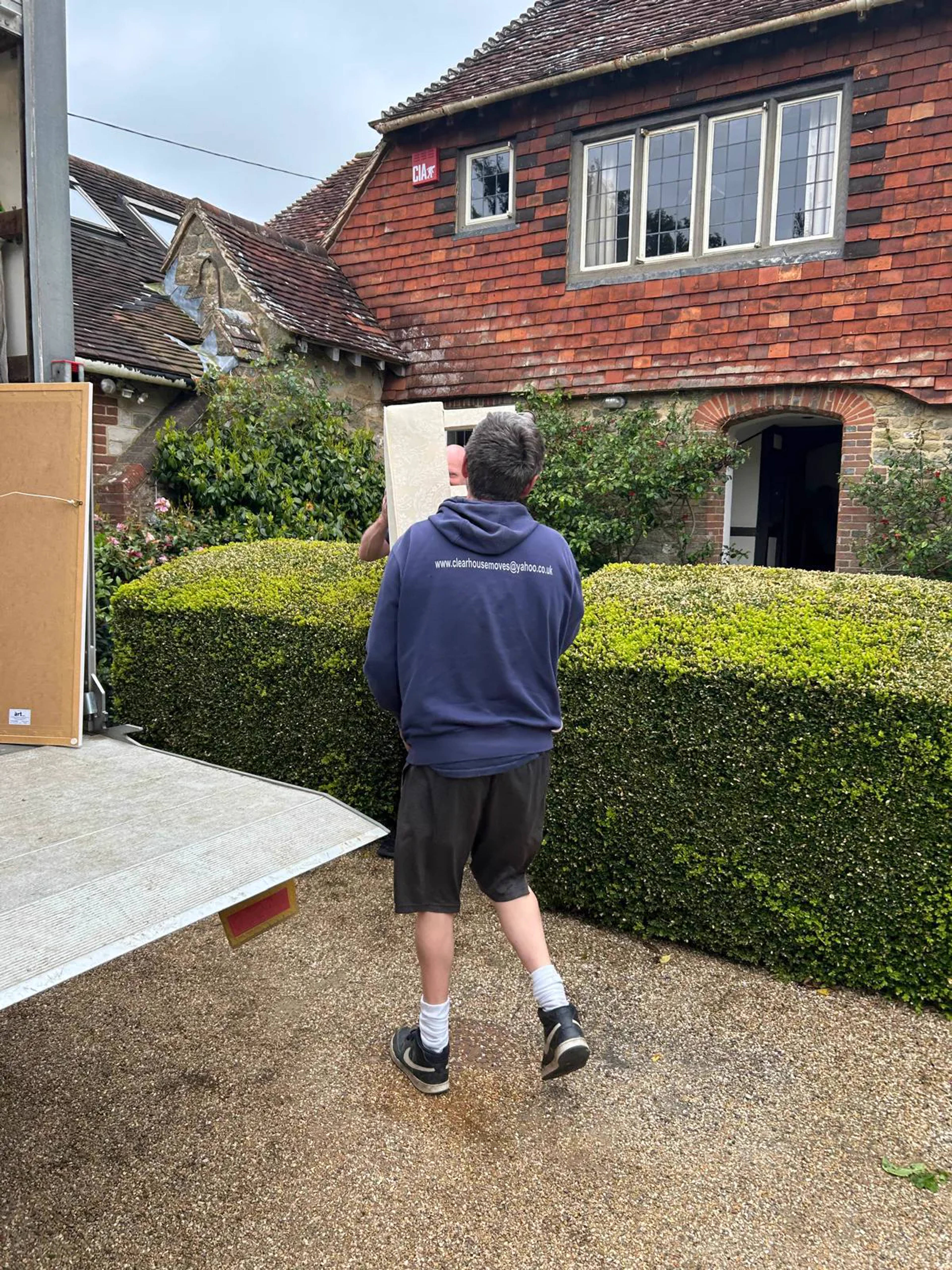 A Clear House Moves team member in branded uniform carrying furniture at a country house