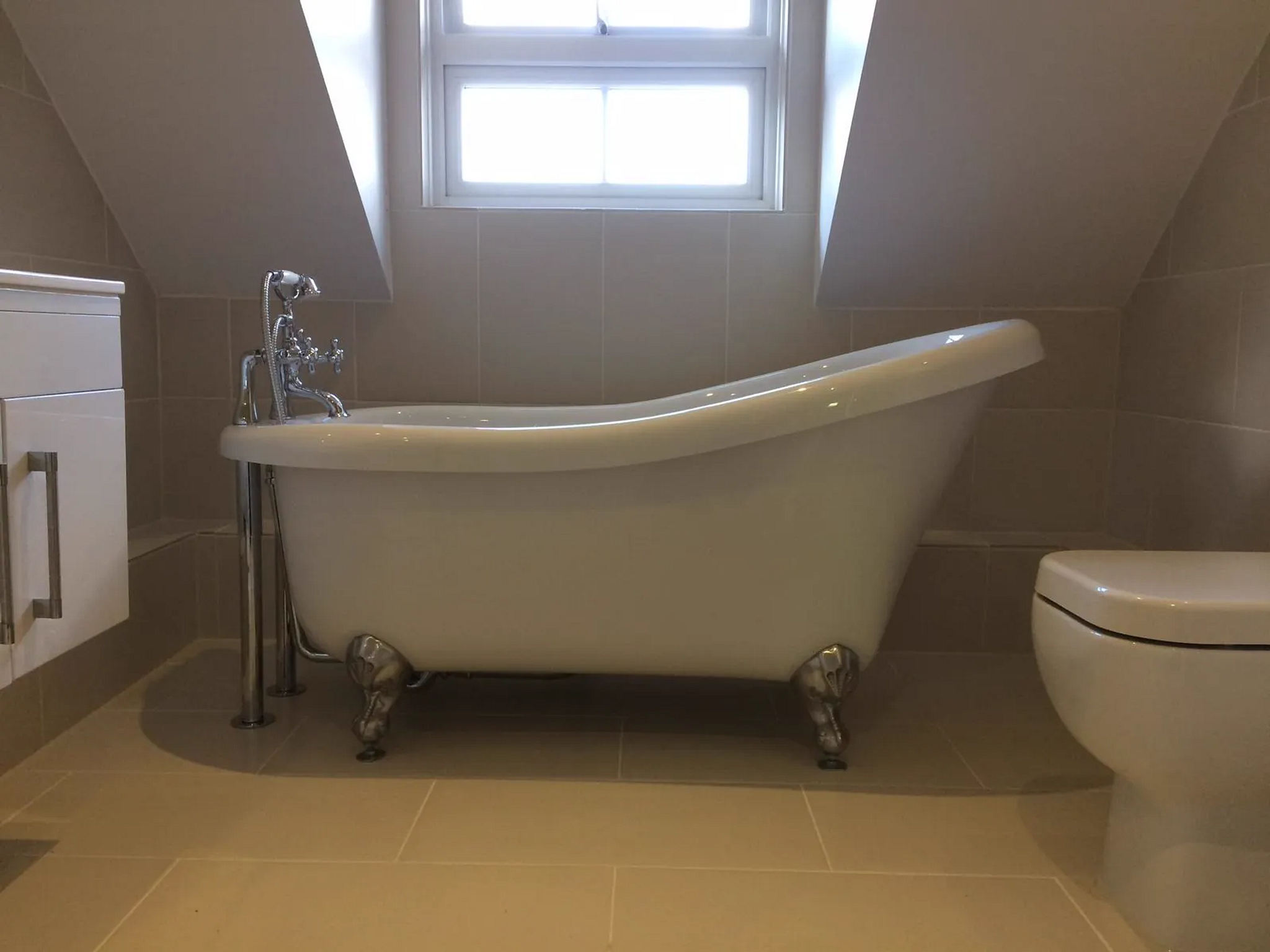 Freestanding slipper bath with chrome claw feet and floor-standing tap in a tiled loft bathroom