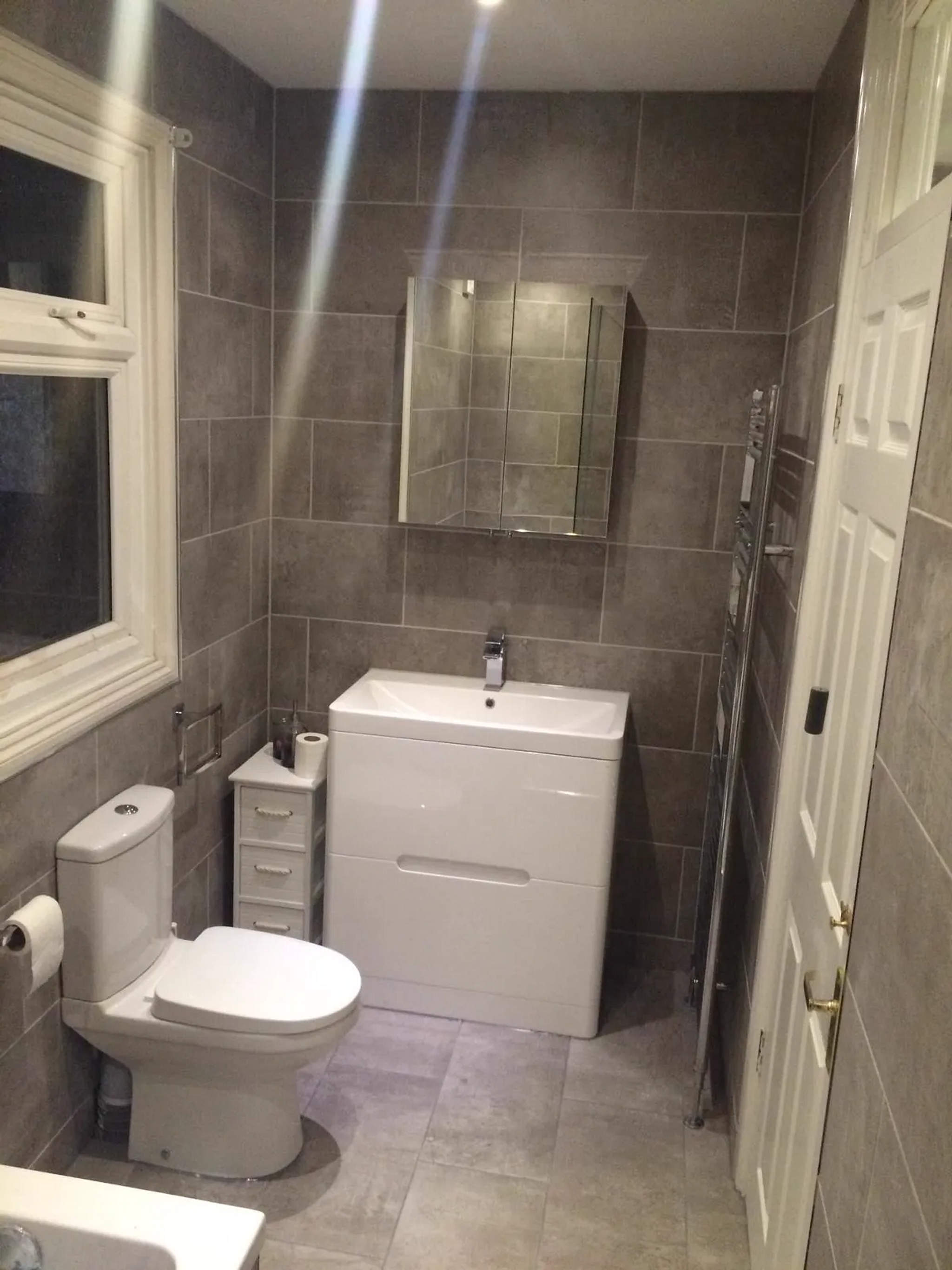 Grey-tiled bathroom with white vanity basin, close-coupled WC and chrome heated towel rail