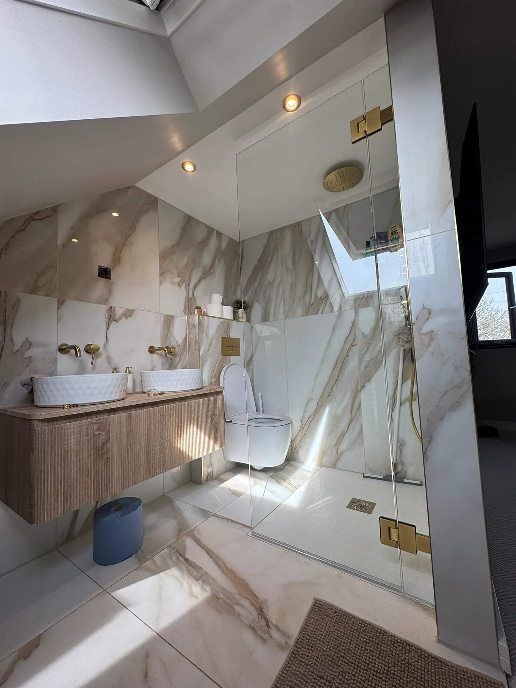 Calacatta marble loft bathroom with twin counter-top basins, brass taps and walk-in shower