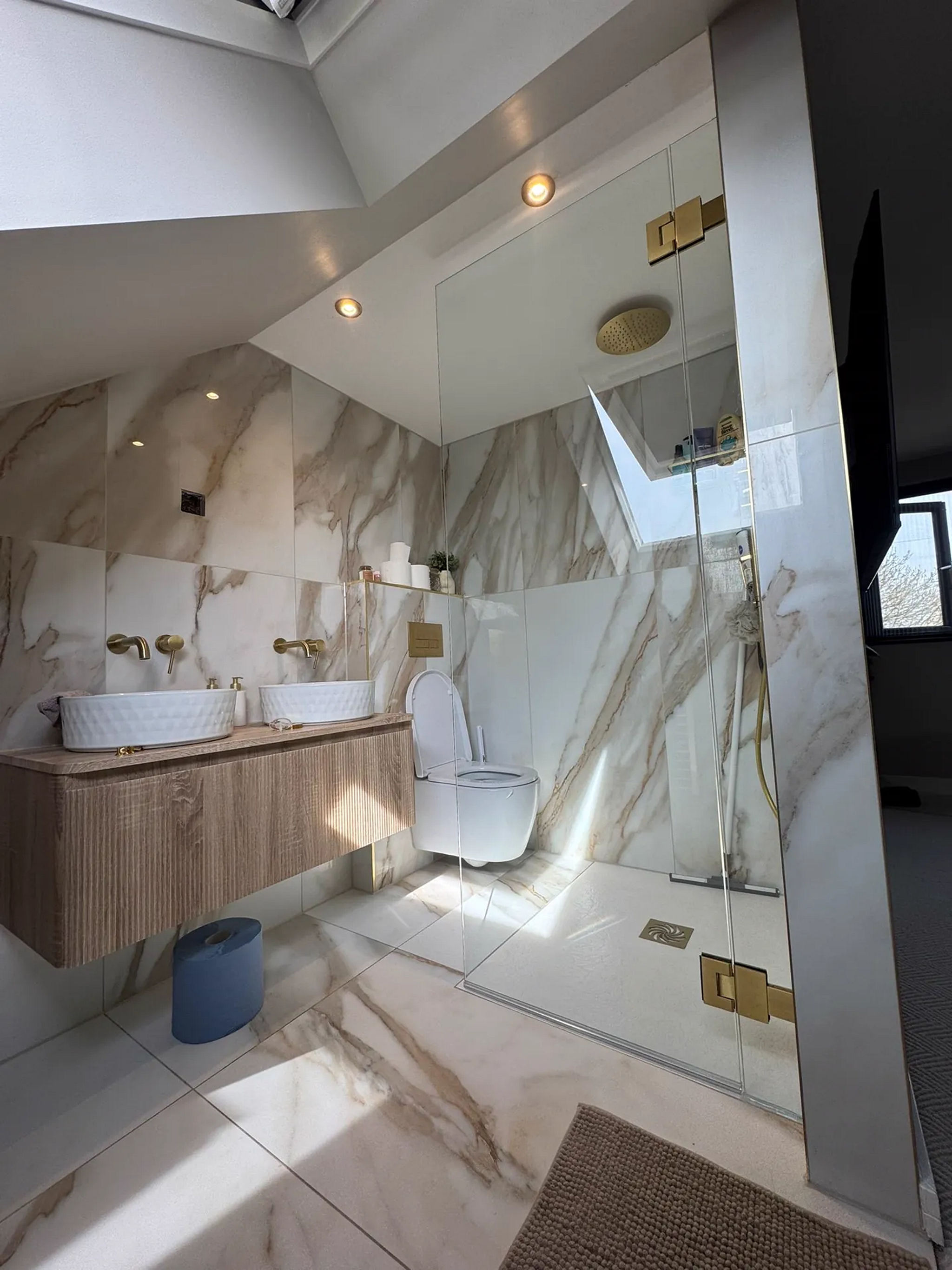 Calacatta marble loft bathroom with twin counter-top basins, brass taps and walk-in shower