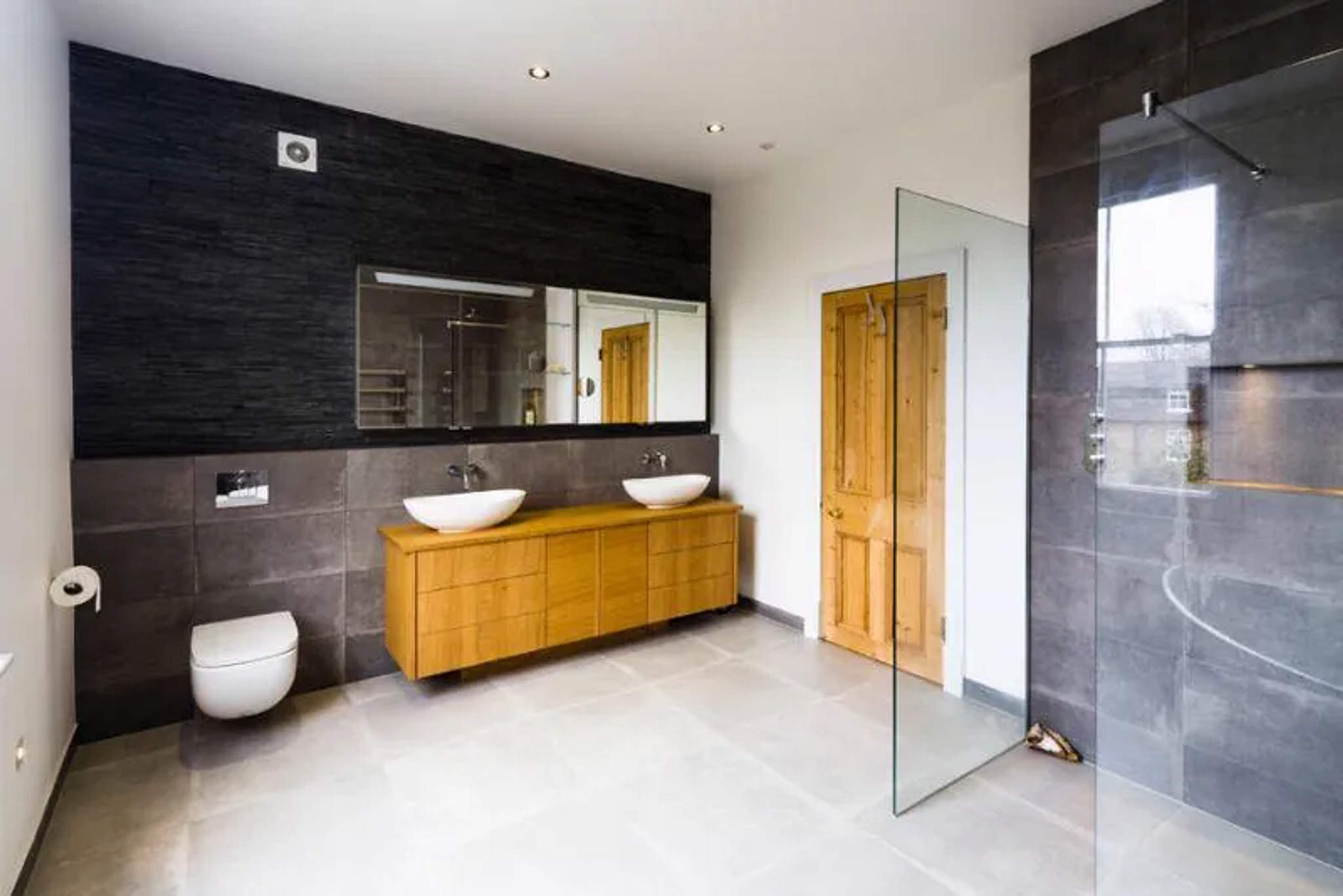 Open-plan bathroom with twin vessel basins on oak vanity, wall-hung WC and glass walk-in shower