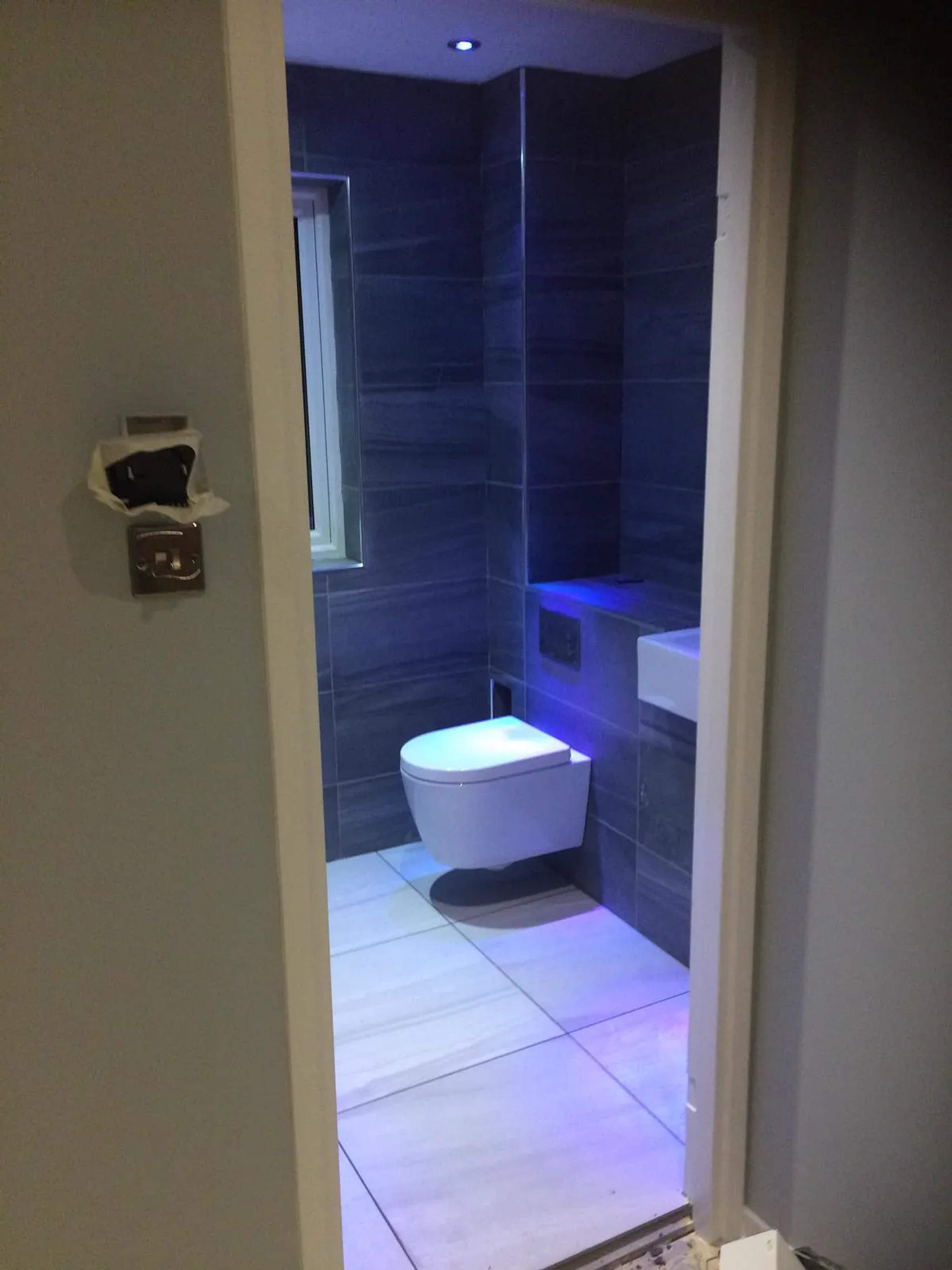 Wall-hung WC in a grey-tiled cloakroom with blue accent lighting and counter-top basin