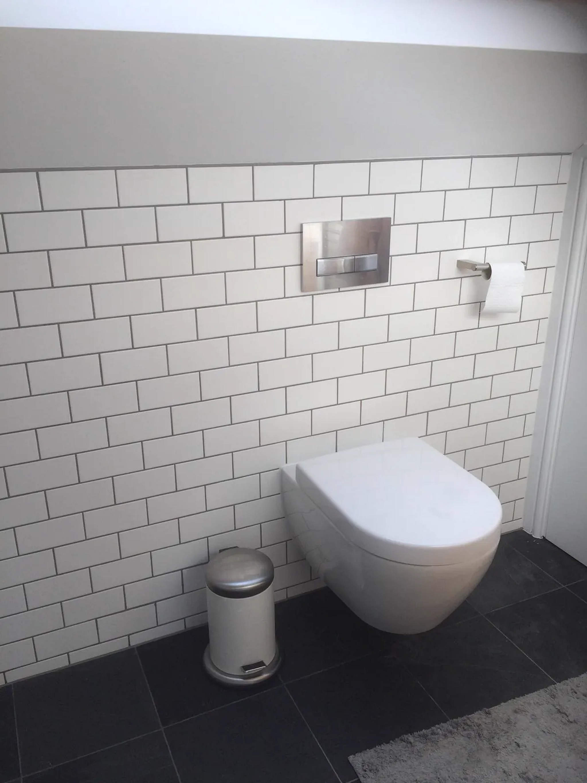 Wall-hung WC with chrome flush plate against white metro tiling and dark slate floor tiles