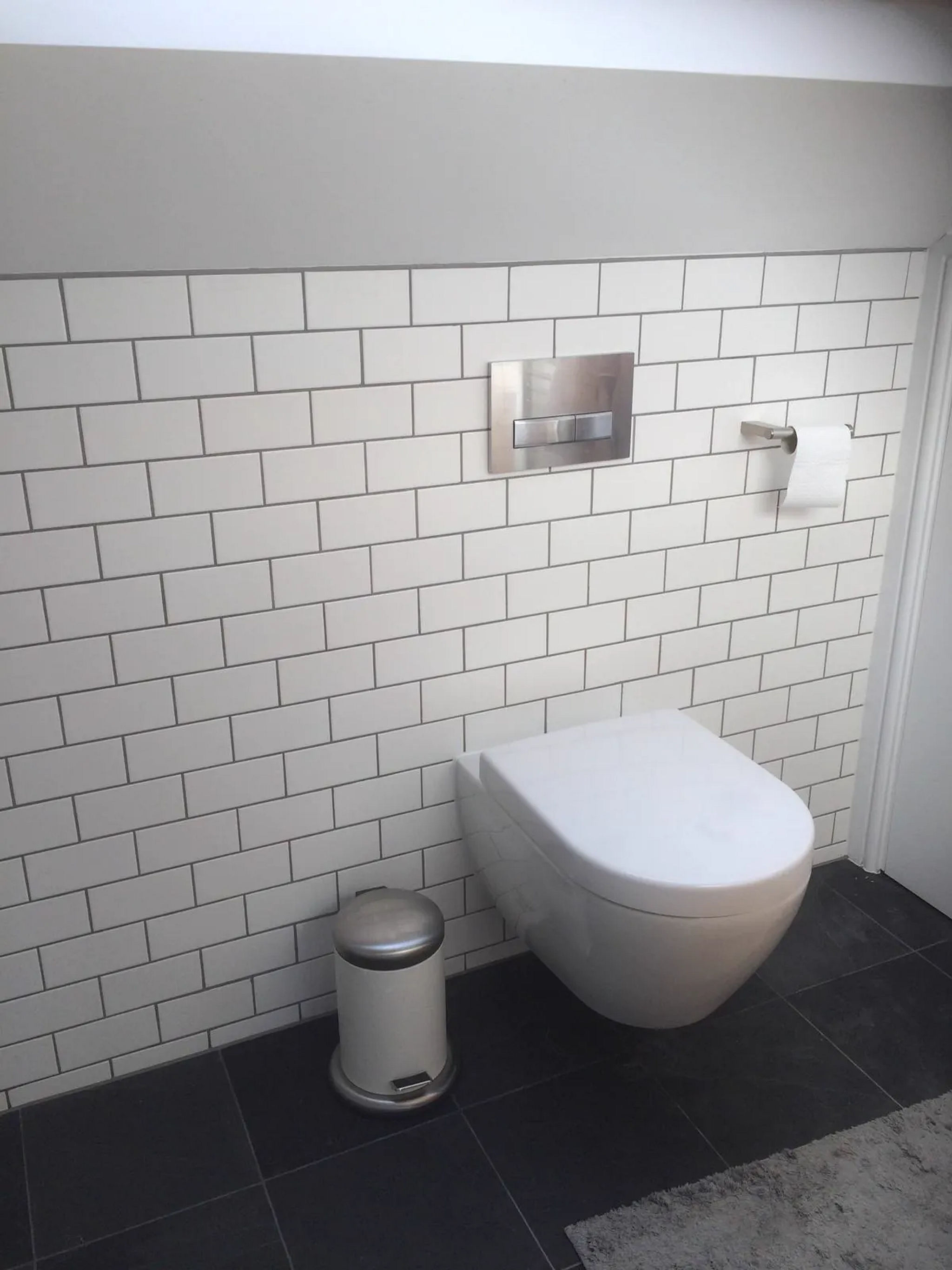 Wall-hung WC with chrome flush plate against white metro tiling and dark slate floor tiles