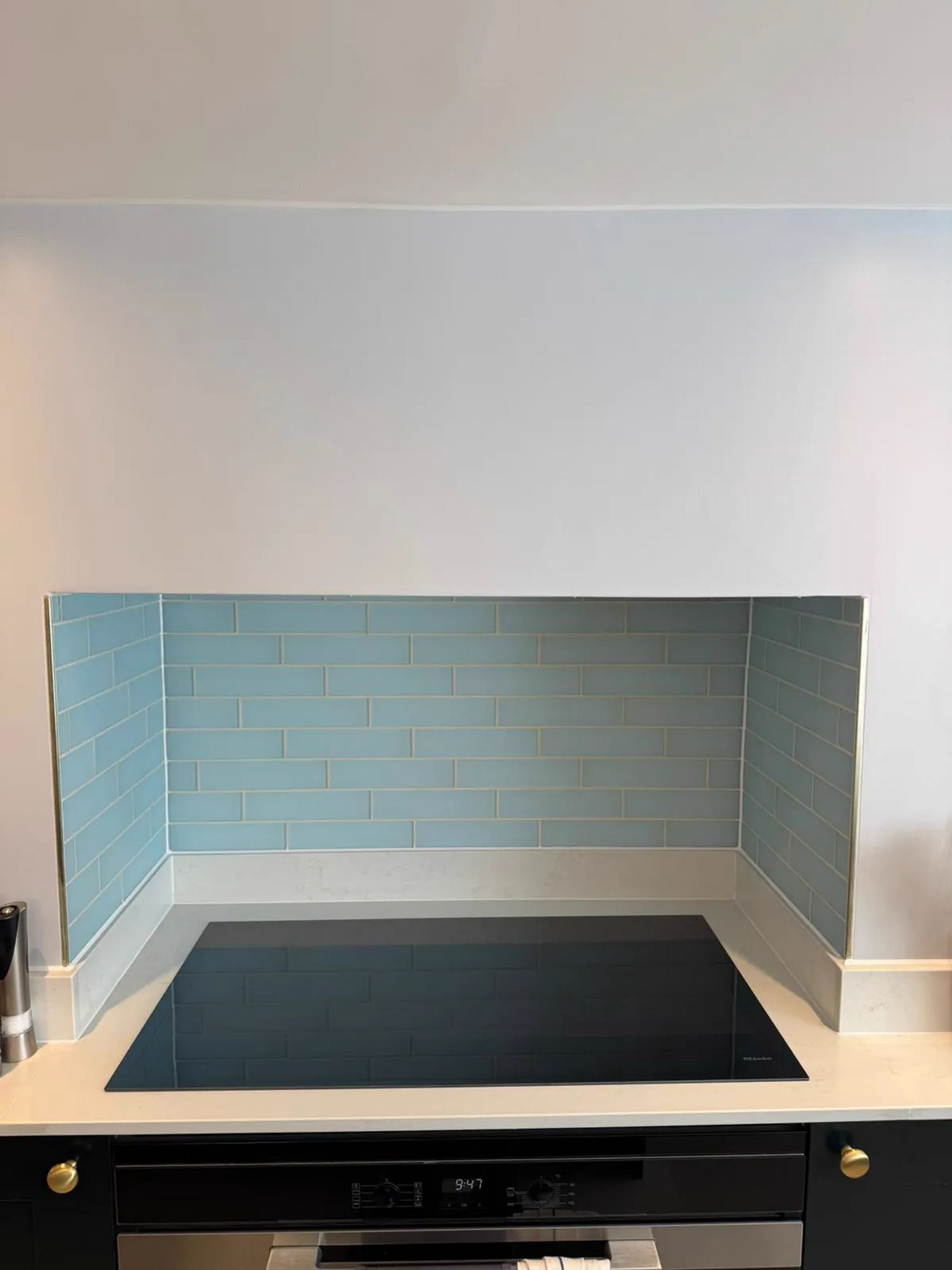 Black induction hob below light blue metro-tile splashback on a cream worktop