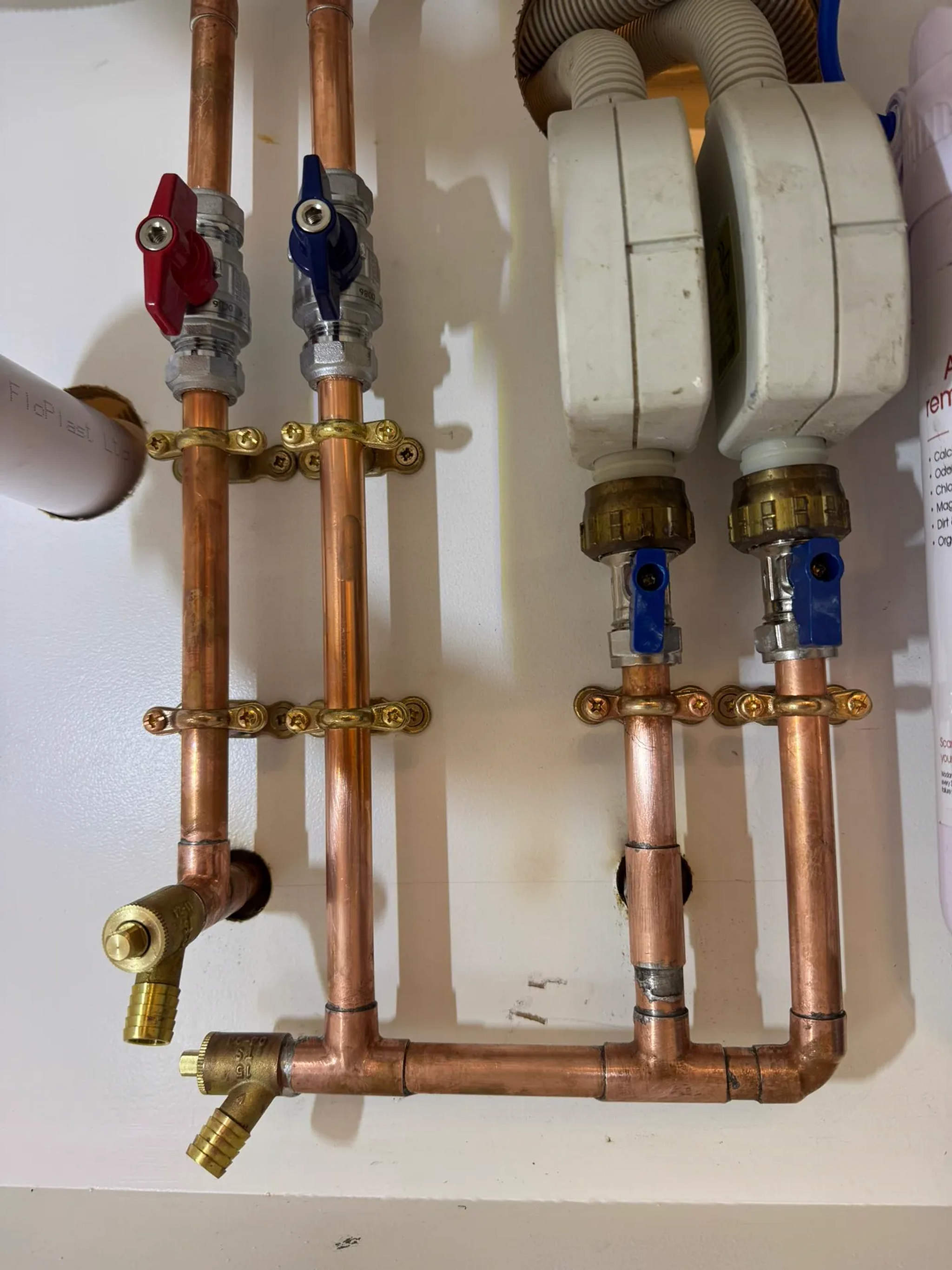 Copper pipework with red and blue isolation valves under a kitchen sink