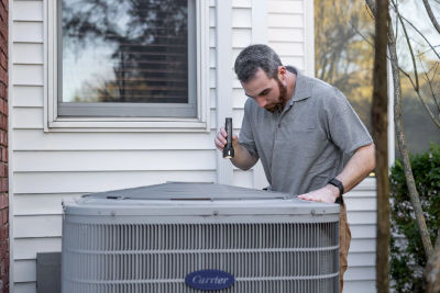 HVAC technician inspecting an outdoor air conditioning unit with a flashlight