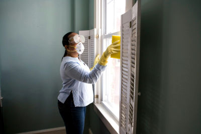 House cleaner in gloves and a mask wiping down a window