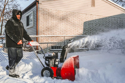 Person clearing a snowy sidewalk with a snowblower