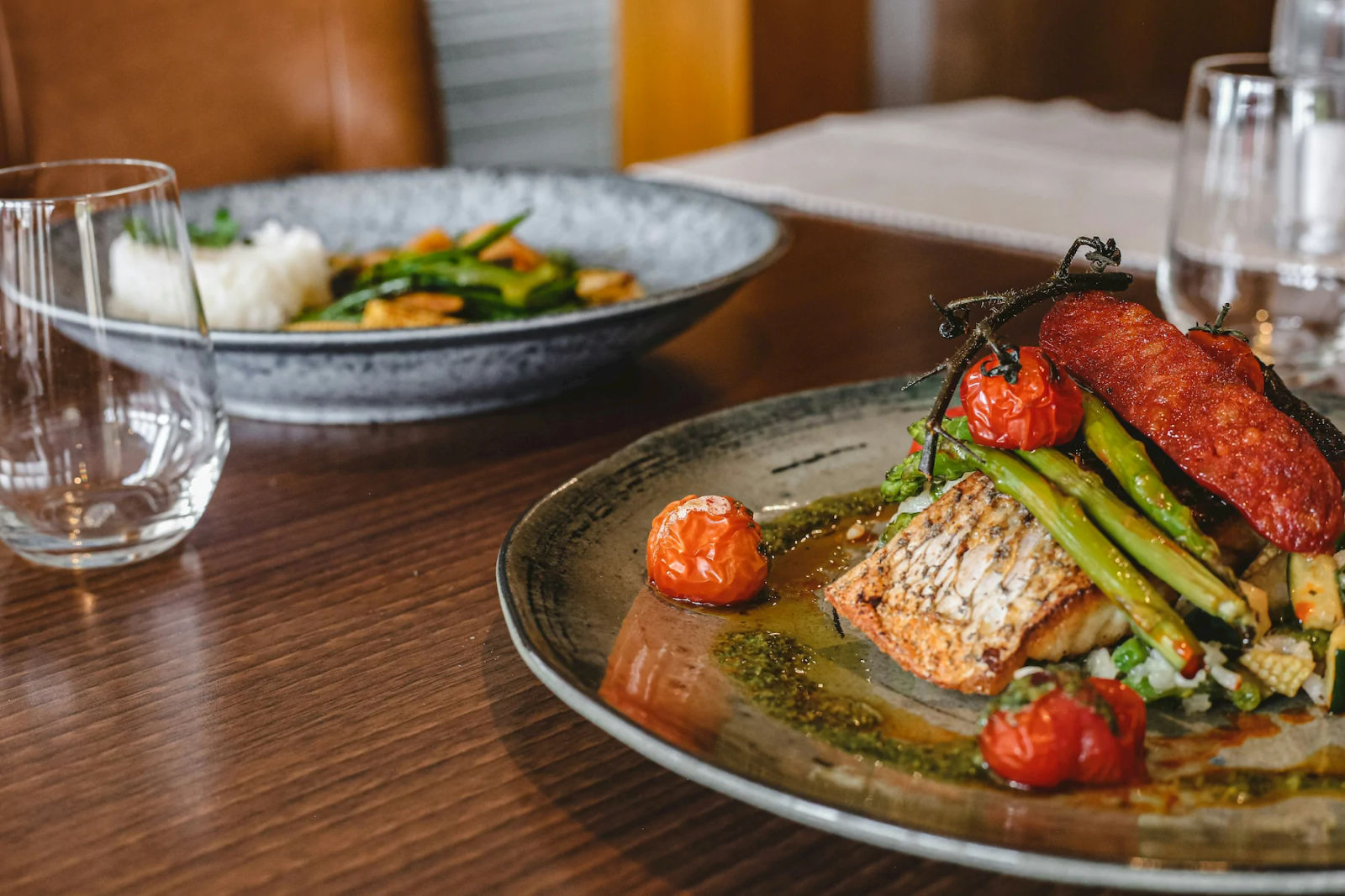 A plated fish dish with roasted tomatoes and asparagus on a wooden restaurant table