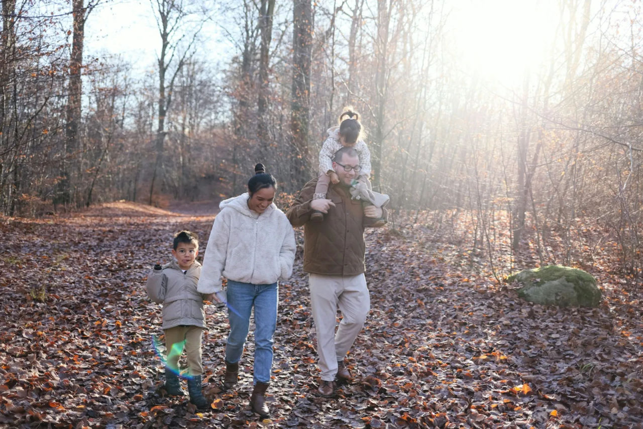 A parent and two children walking a leaf-covered path in the woods