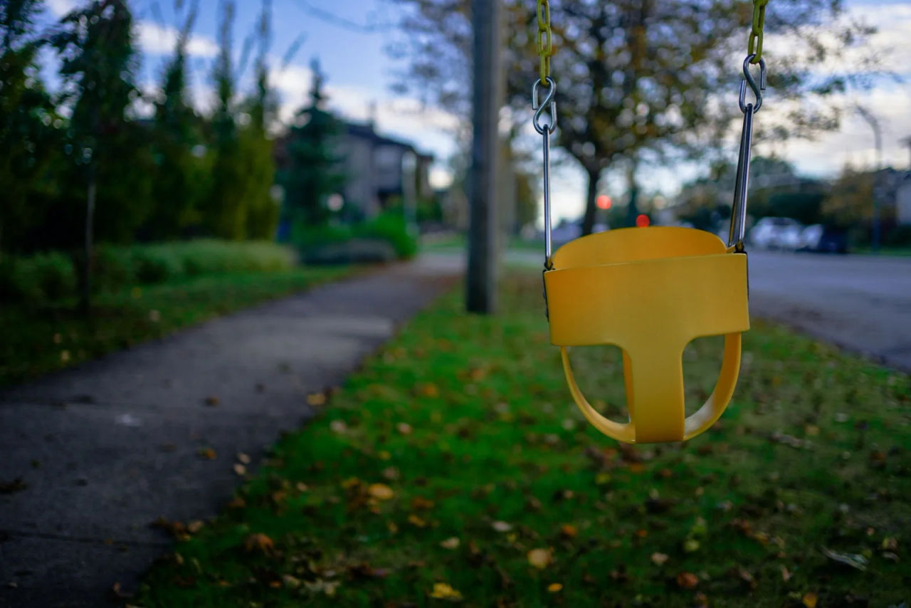 An empty child’s swing hanging beside a suburban footpath at dusk