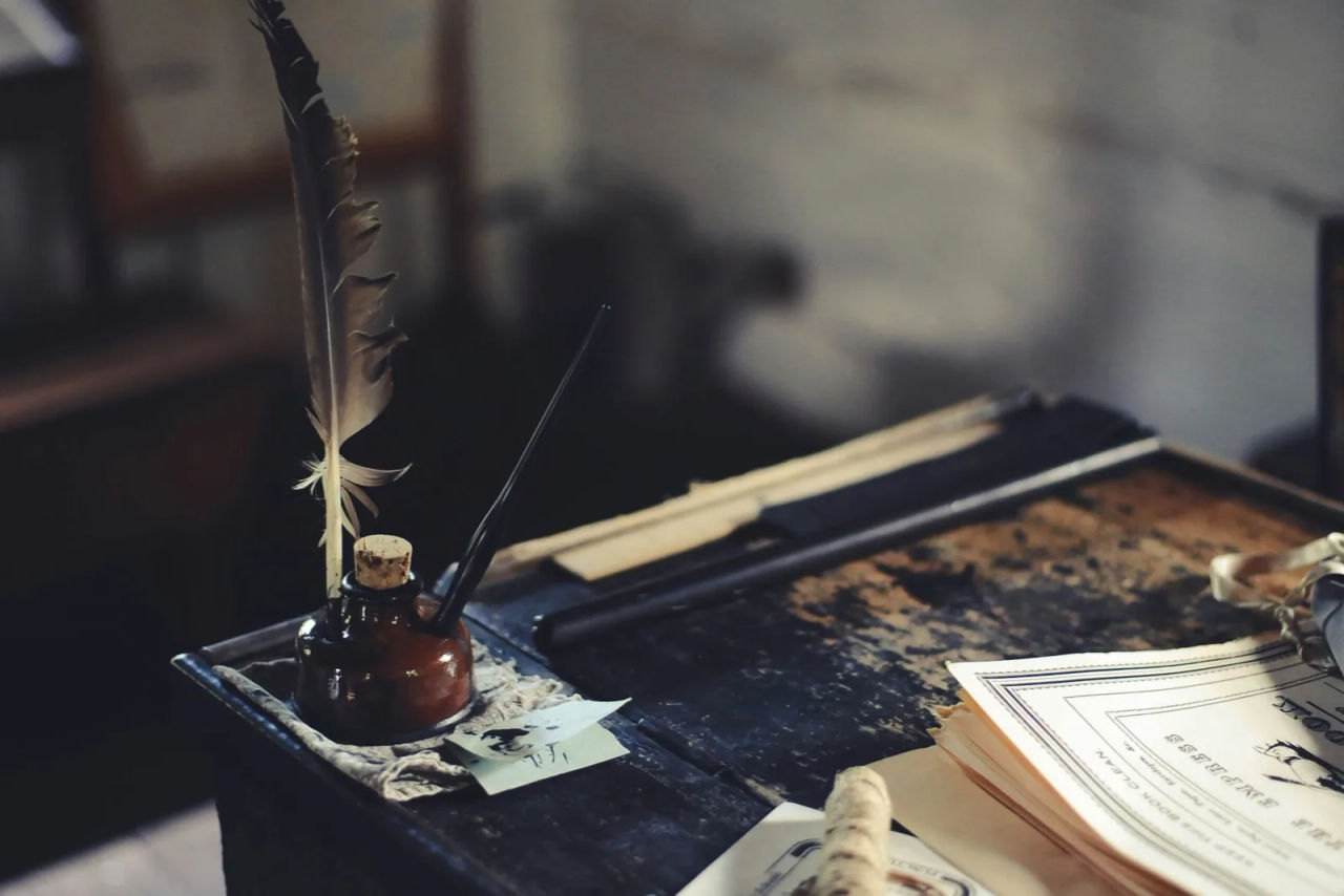 A quill pen and inkwell on a desk with old documents