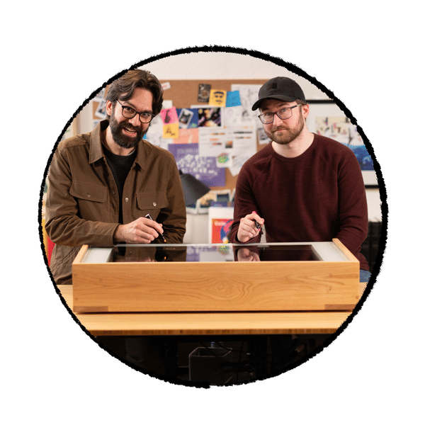 Two BibleProject animators sitting at a desk with visual aids.