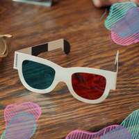 Photo of paper 3D glasses with red and cyan lenses on a wooden table, with overlapping color accents.