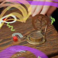 Photo of a horseshoe magnet and a brass compass on a wooden table, with colorful streamer accents.