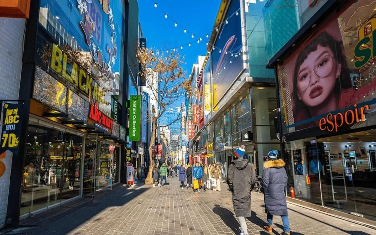 Myeongdong shopping street during the day with blue skies and travelers strolling between major stores.