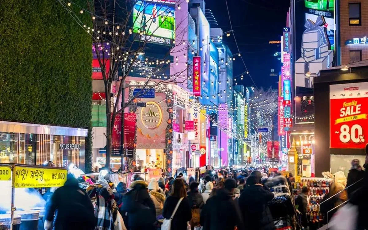 Myeongdong at night illuminated by colorful Korean signboards and lively pedestrian crowds.