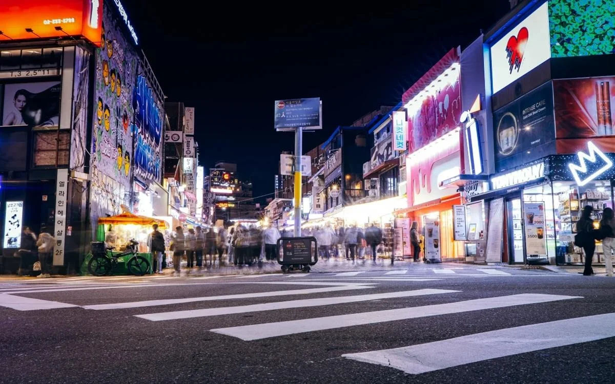 Seoul street at night illuminated by neon lights with bustling pedestrians and bright storefronts.