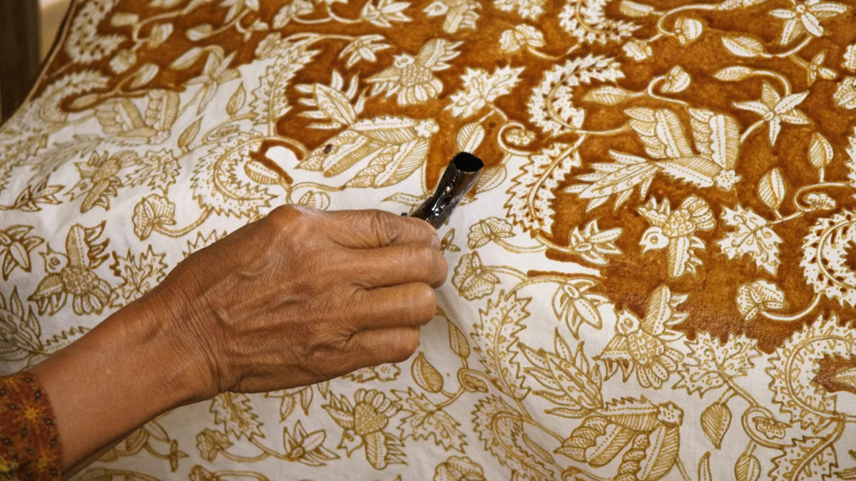 An artisan hand-drawing patterns on Batik fabric
