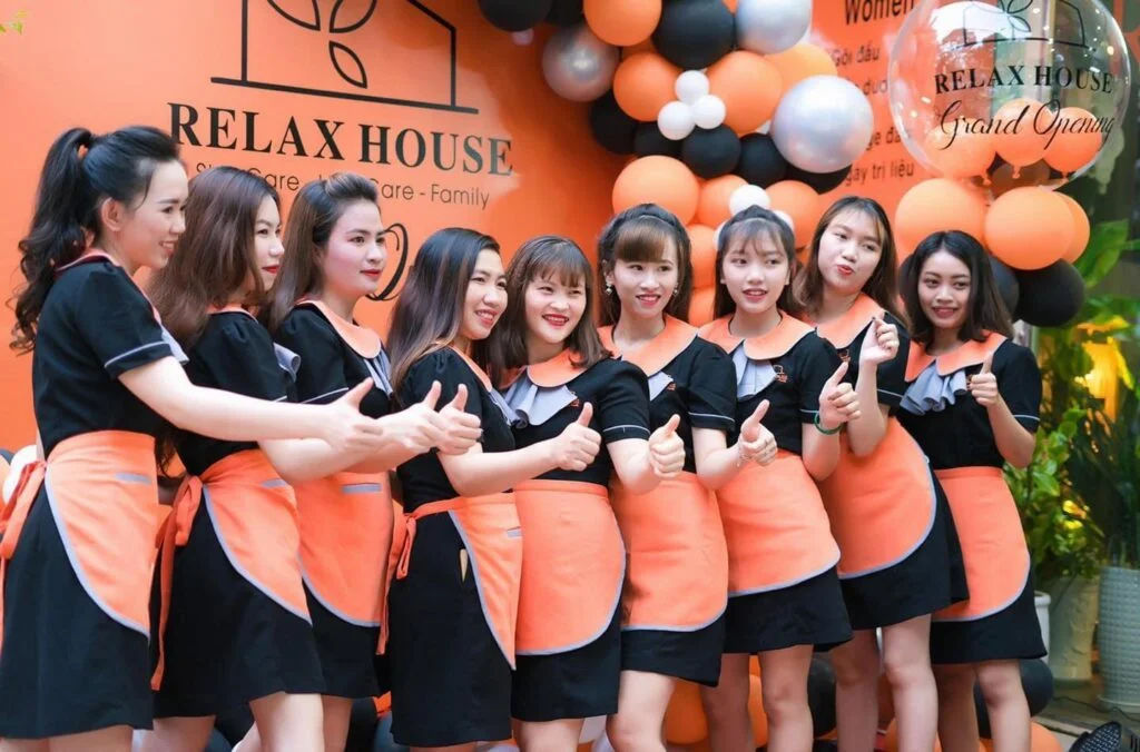 Đội ngũ spa mặc đồng phục chụp ảnh tại sự kiện khai trương với backdrop thương hiệu