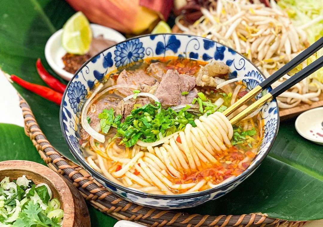 A bowl of Bun Bo Hue with thick noodles, rich broth, beef, sausage, and pork hock