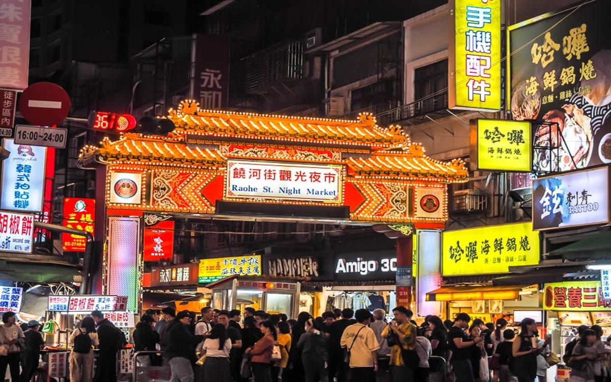 The Raohe Night Market gate was brightly lit, with crowds of people standing and walking in front of it.