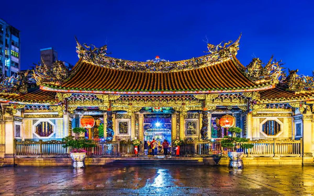 Taipei's Longshan Temple shines brightly with its ancient tiled roof and lights reflecting on the wet bricks.