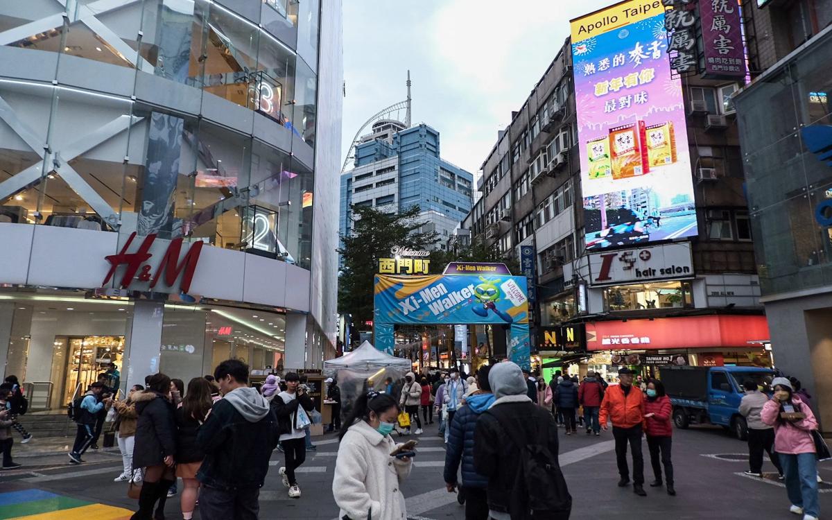 The scene in Ximending is bustling with pedestrians, large billboards, and a prominent H&M store.