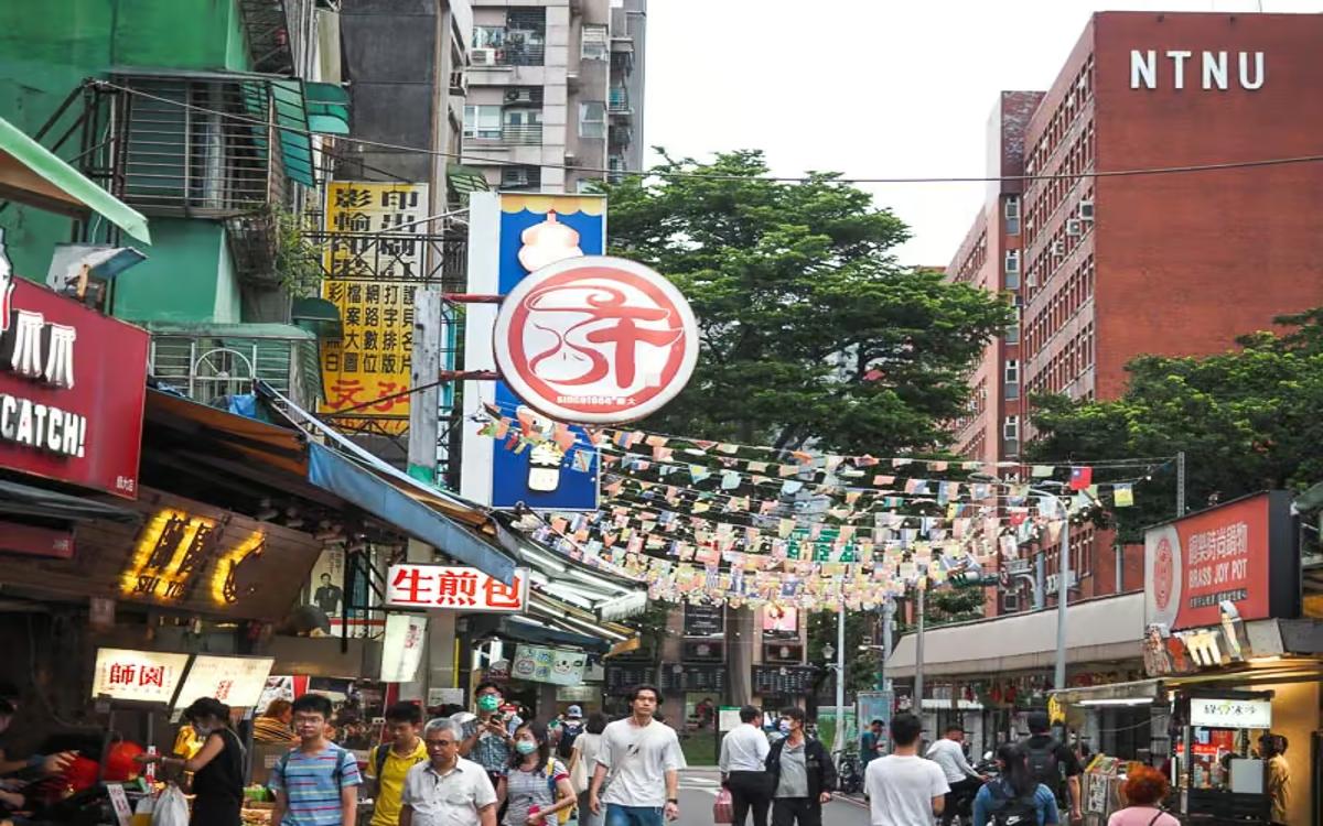 The street near NTNU is lined with stalls, Chinese signs, and is bustling with pedestrians.