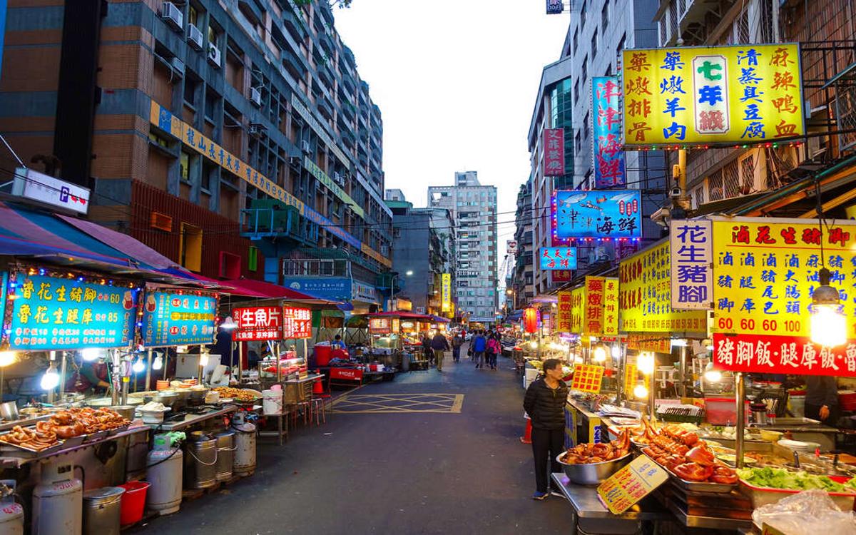 Taipei's night market street is lined with stalls, brightly lit signs, and pedestrians on both sides.