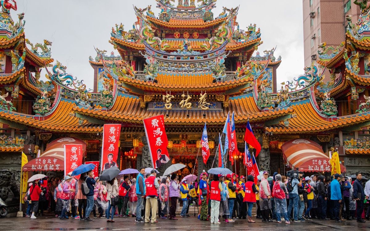 Hình ảnh Chùa Từ Hựu với mái ngói cong nhiều tầng, trang trí rồng phượng sặc sỡ, phía trước là đông người che ô trong ngày mưa.