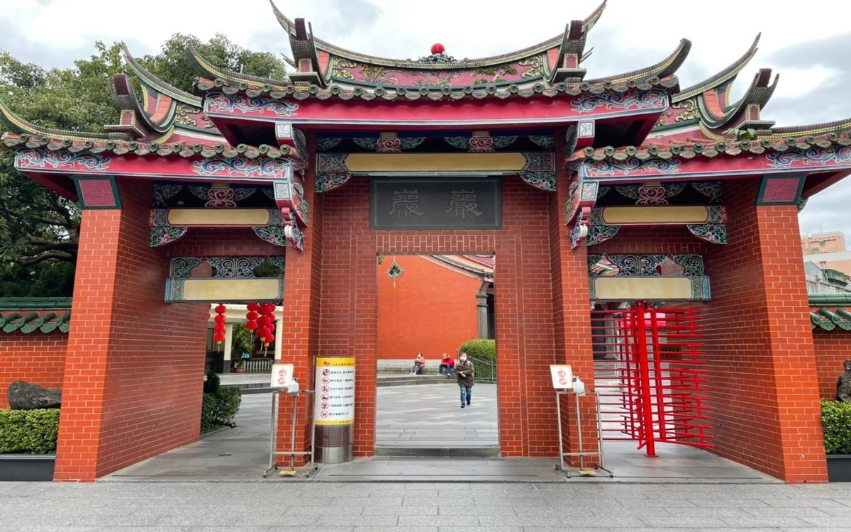 Cổng đền gạch đỏ với bảng chữ “康樂” trên mái cong chạm trổ tinh xảo, dẫn vào khuôn viên bên trong nơi du khách ra vào.
