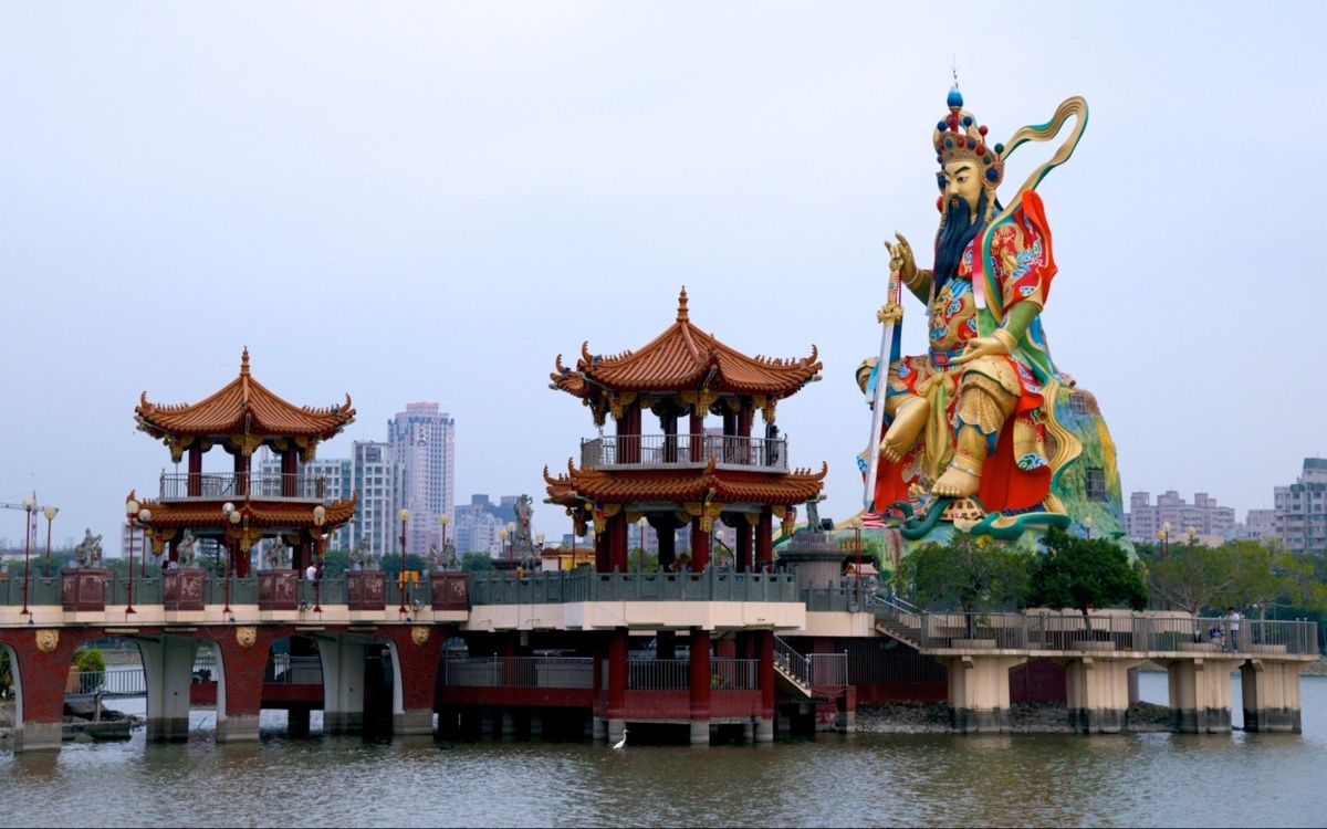 Hình ảnh đền ở Đài Bắc với các mái đình truyền thống trên hồ và tượng thần khổng lồ đầy màu sắc phía sau.